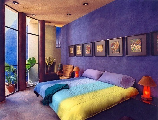 interior-design-for-colorful-bedroom-with-colorful-blanket-and-pillows-also-two-desk-lamps-and-wooden-arm-chair-also-windowed-wall-also-some-paintings-on-frame-also-blue-wall-915x692